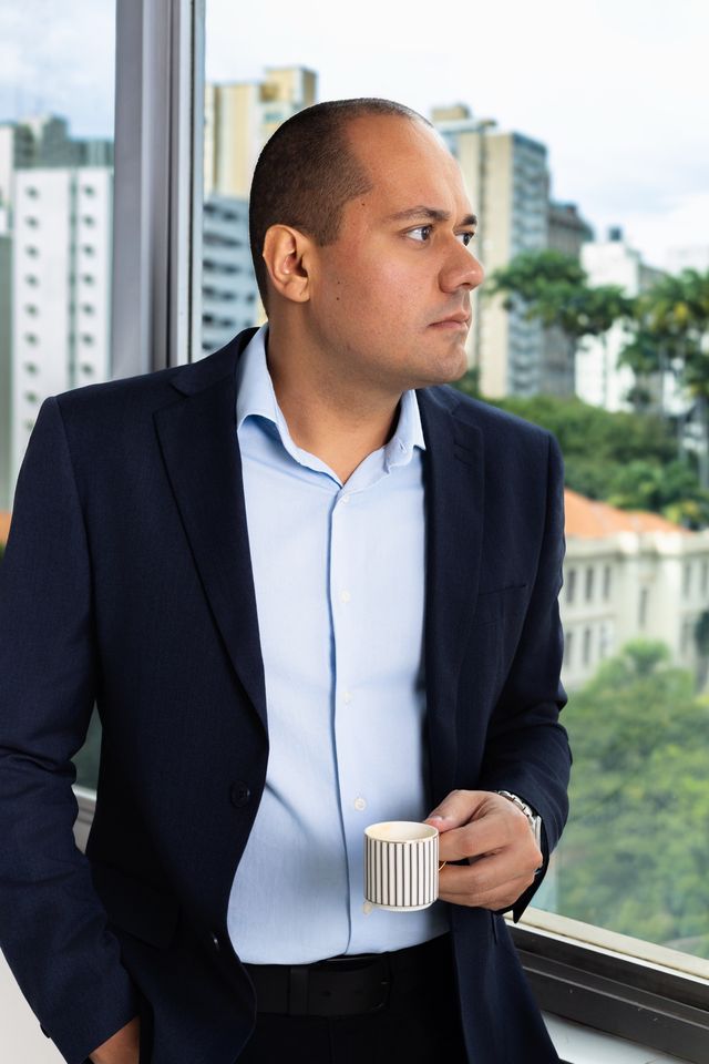 Matheus Marques olhando pela janela, com uma xícara de café