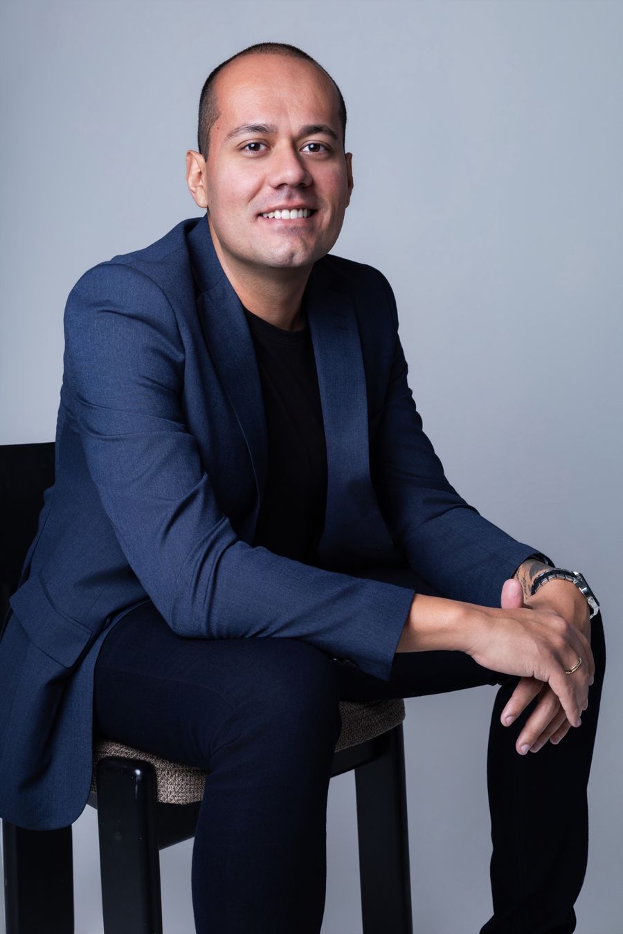Matheus Marques sorrindo, sentado, de blazer azul-marinho